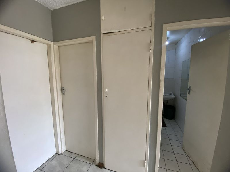 A functional hallway featuring built-in storage cupboards and tiled flooring, providing access to adjacent rooms including a bathroom.