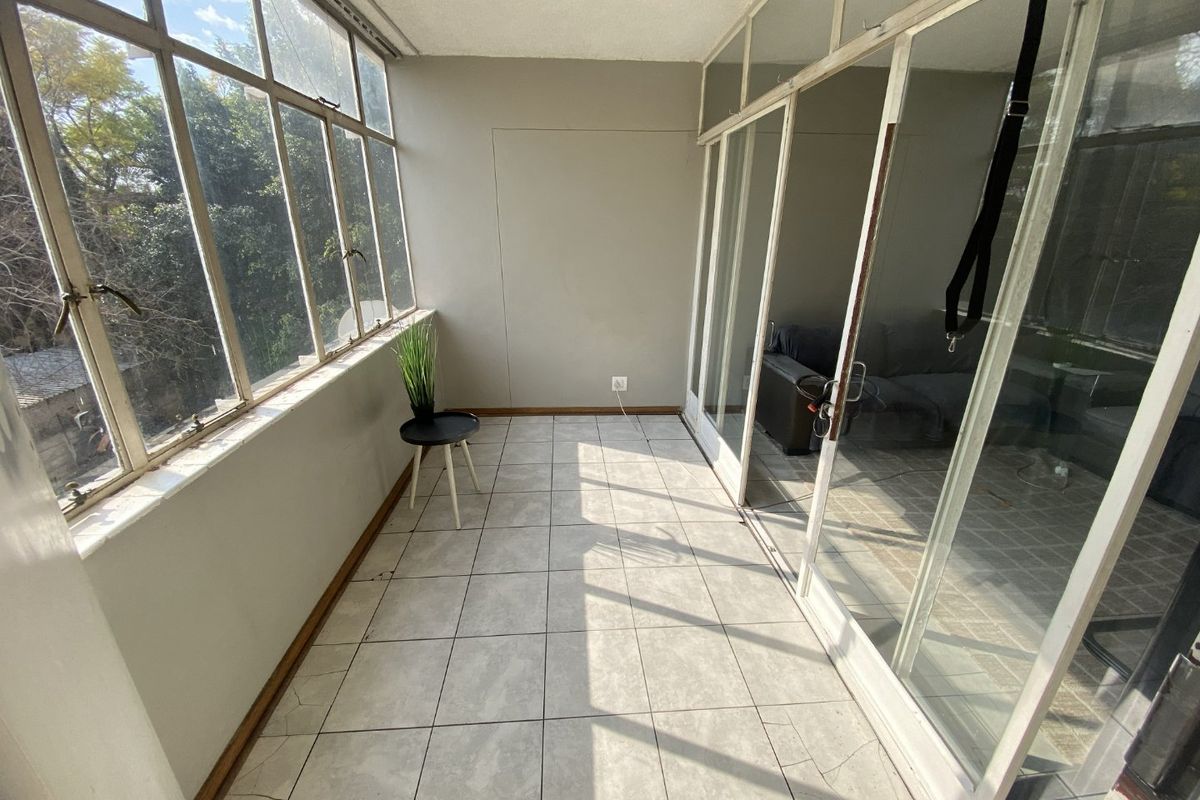 Enclosed balcony or sunroom featuring tiled flooring, large windows, and sliding glass doors, offering a bright and versatile space.