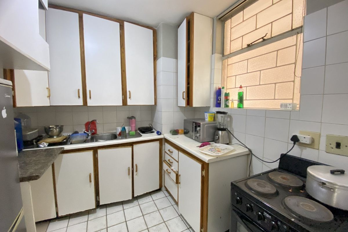 A functional kitchen featuring white cabinetry, laminate countertops, tiled backsplash, and tiled flooring, offering a dated aesthetic ready for modernization.