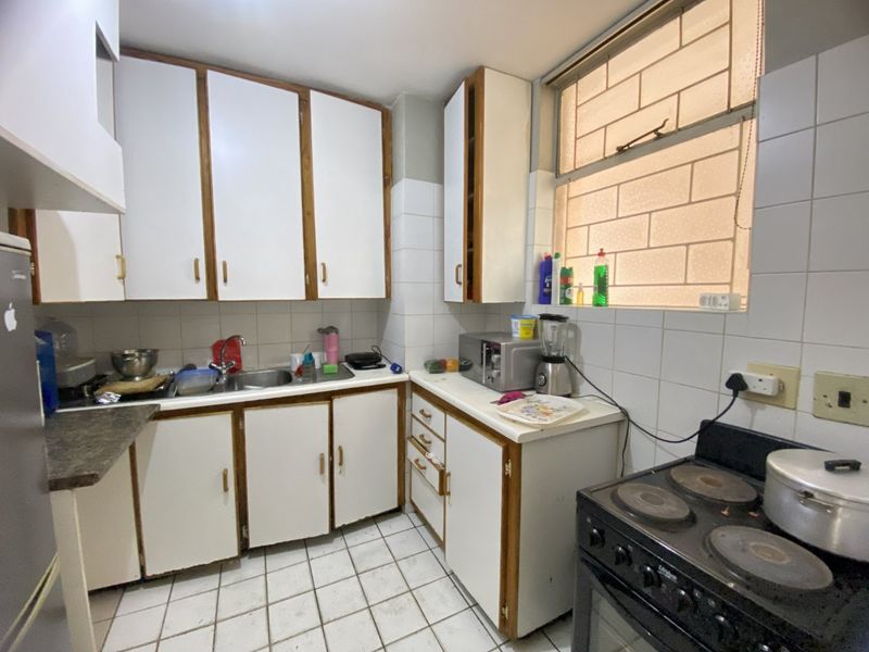 A functional kitchen featuring white cabinetry, laminate countertops, tiled backsplash, and tiled flooring, offering a dated aesthetic ready for modernization.