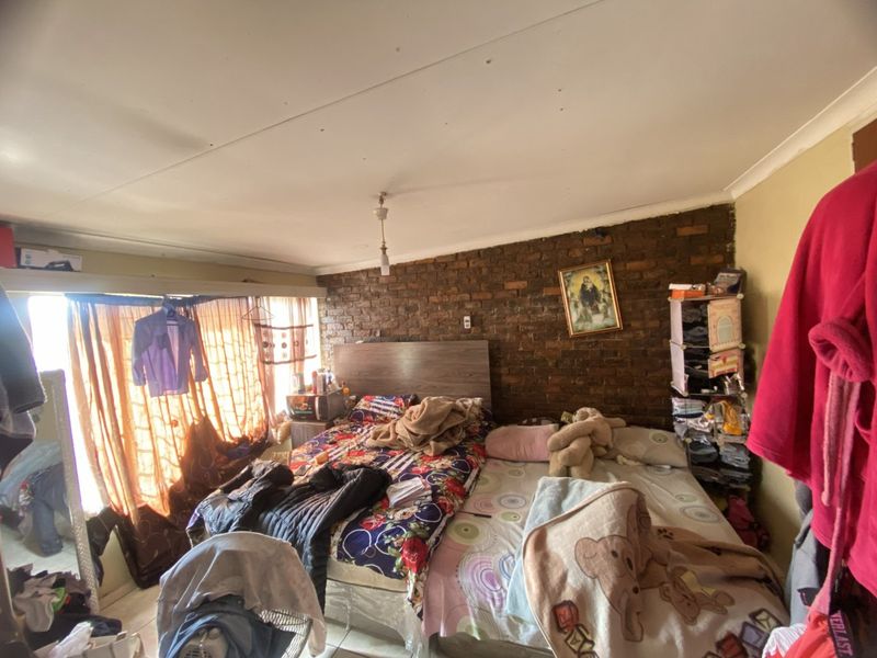 Bedroom featuring an exposed brick feature wall and standard ceiling finishes, requiring cosmetic updates to improve the overall aesthetic and condition.