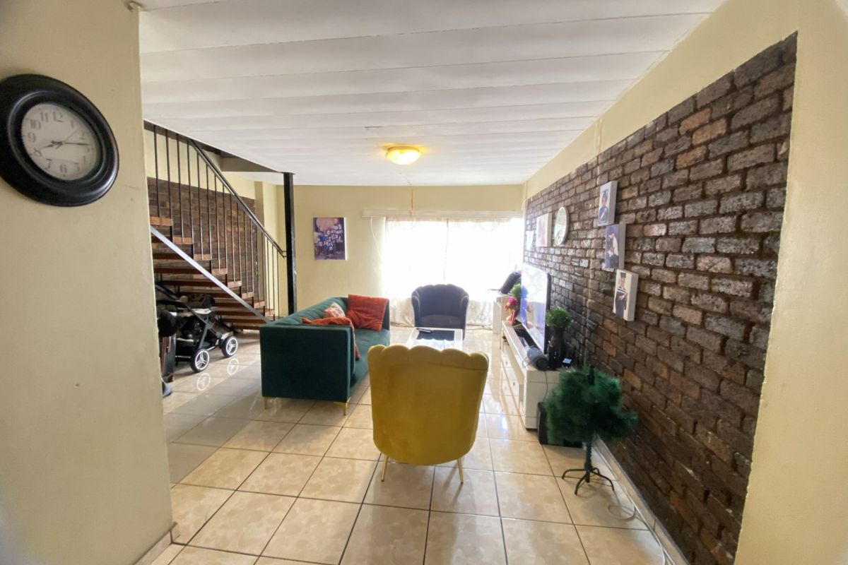 Living room featuring an exposed brick wall, tiled flooring, and an internal staircase with metal railings.