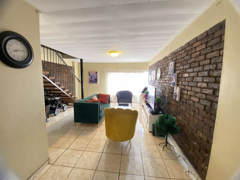 Living room featuring an exposed brick wall, tiled flooring, and an internal staircase with metal railings.