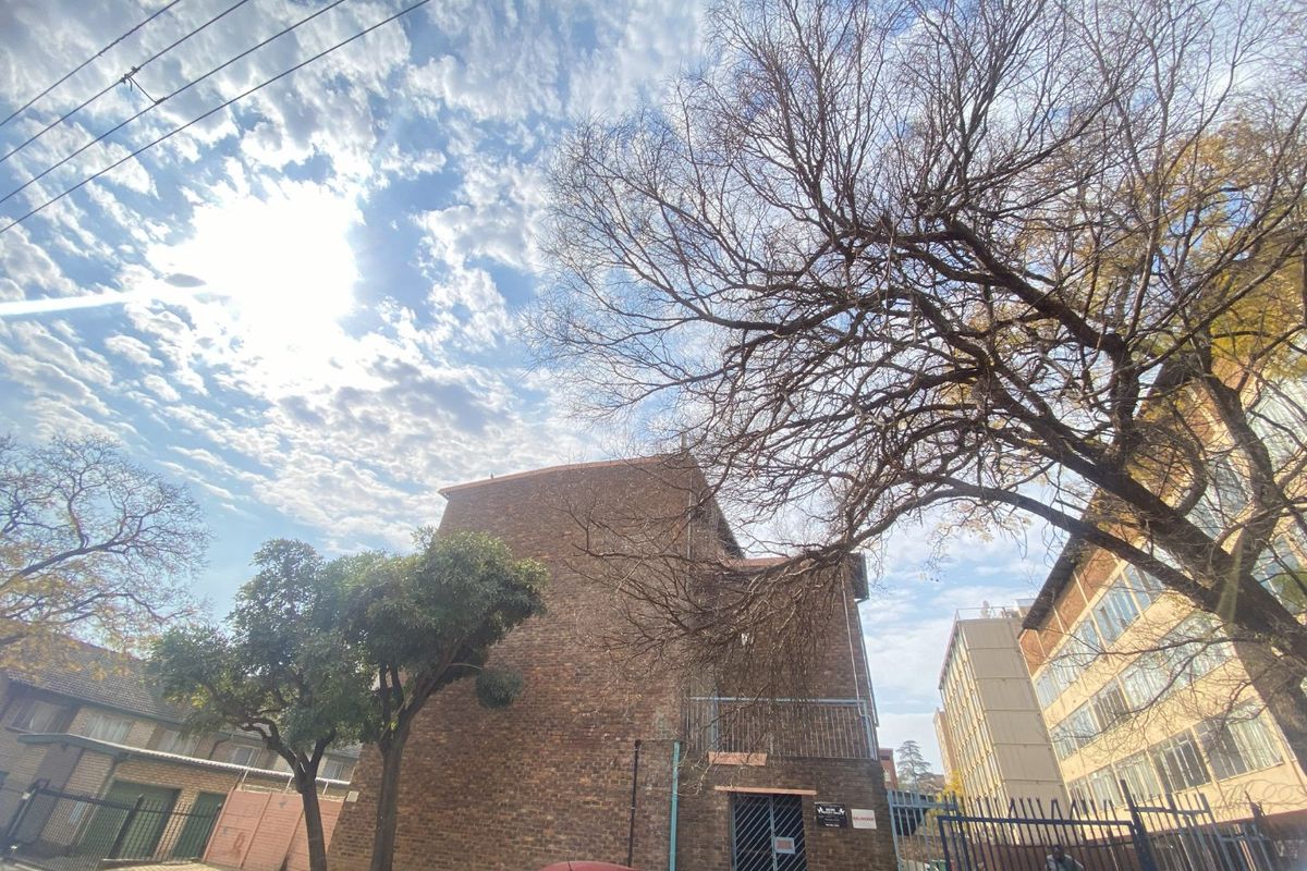 Rear view of the apartment building featuring a brick facade, metal security gate, and balcony access.