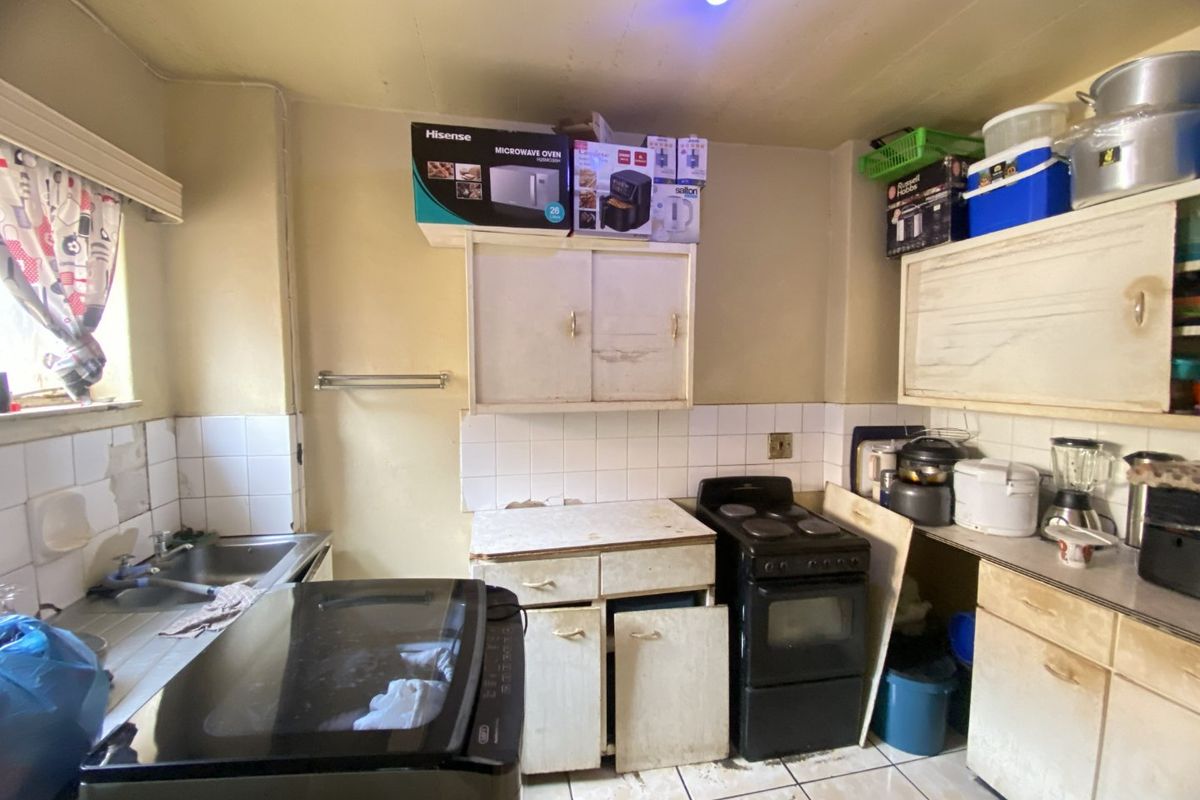A dated kitchen featuring original cabinetry, tiled backsplash, and a freestanding stove, requiring significant renovation and modernization to improve functionality and aesthetic appeal.
