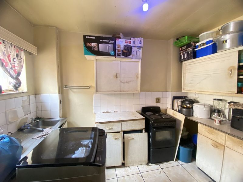 A dated kitchen featuring original cabinetry, tiled backsplash, and a freestanding stove, requiring significant renovation and modernization to improve functionality and aesthetic appeal.