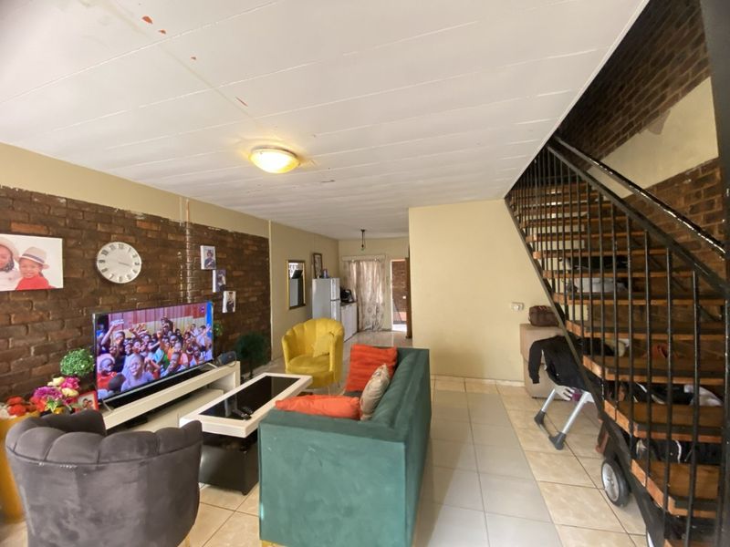 Living room featuring exposed brick walls, tiled flooring, and an internal staircase with metal railings, offering a rustic industrial aesthetic.