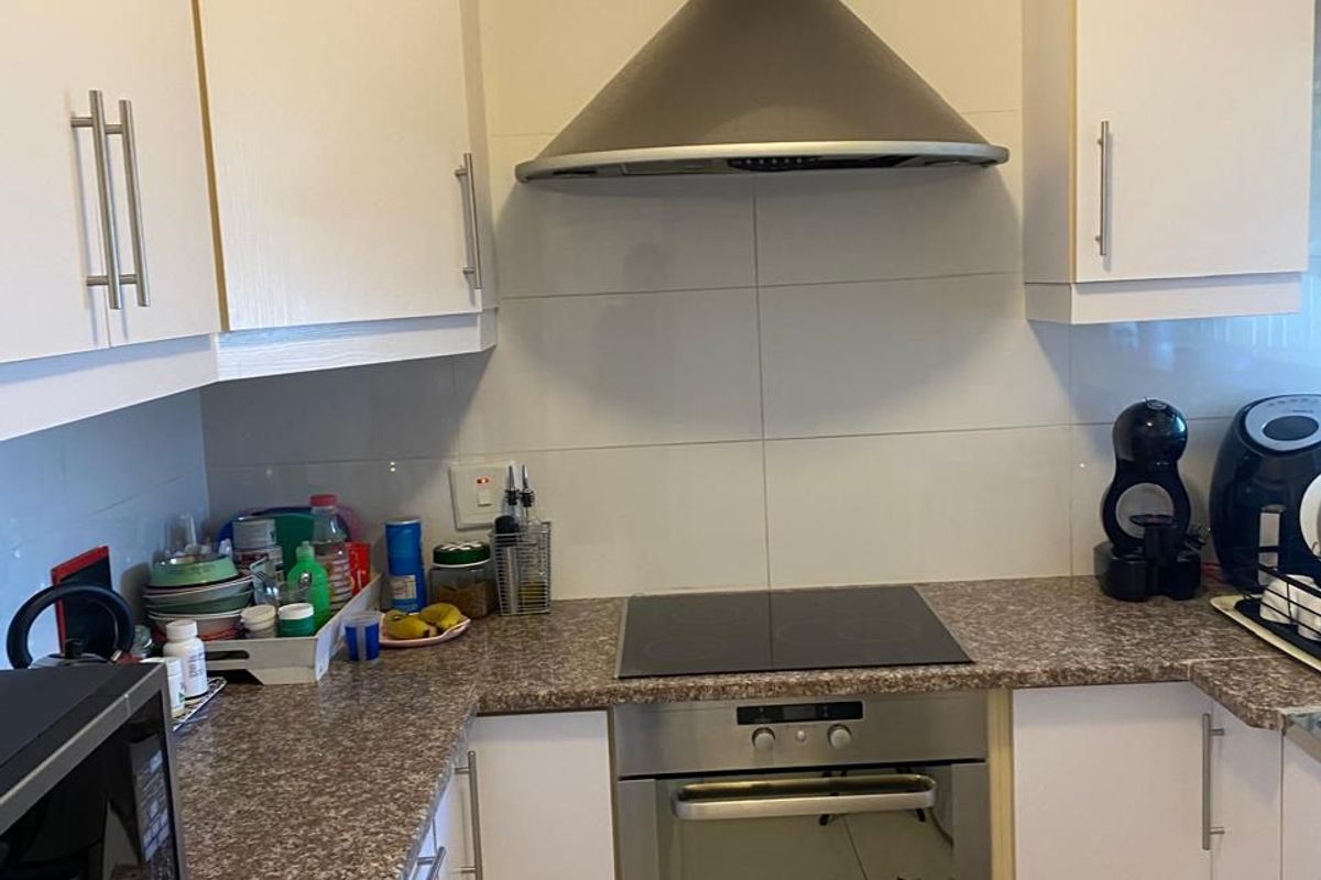 Compact kitchen featuring white cabinetry, granite-look laminate countertops, stainless steel oven, electric hob, and a modern extractor fan with tiled backsplash.