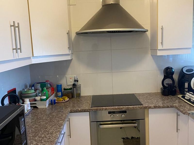 Compact kitchen featuring white cabinetry, granite-look laminate countertops, stainless steel oven, electric hob, and a modern extractor fan with tiled backsplash.