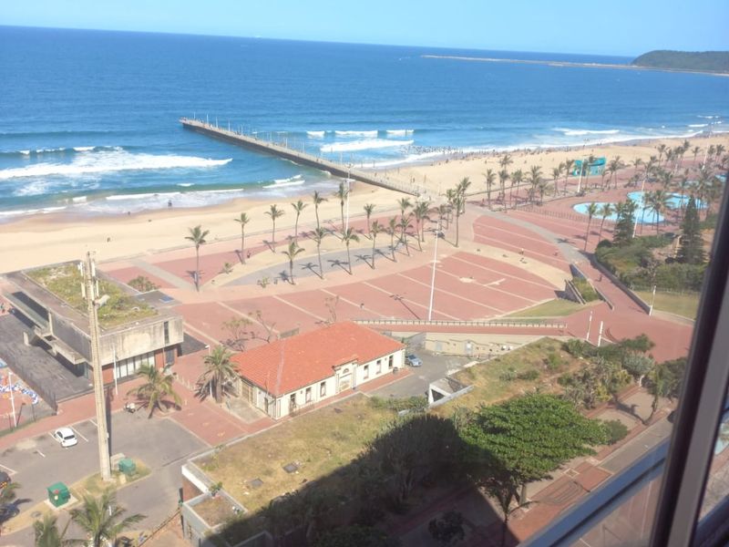 Elevated coastal view overlooking the beach, promenade, and ocean, captured from an apartment window.