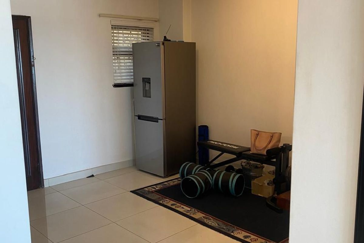 A neutrally painted living area featuring tiled flooring, a window with venetian blinds, and ceiling-mounted spotlighting, offering a versatile space for various uses.