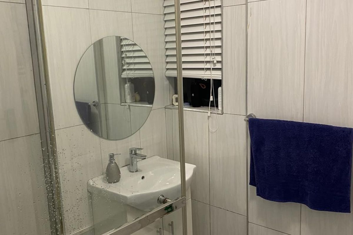A compact bathroom featuring floor-to-ceiling wall tiles, a modern vanity unit with a basin, and a glass-enclosed shower area.