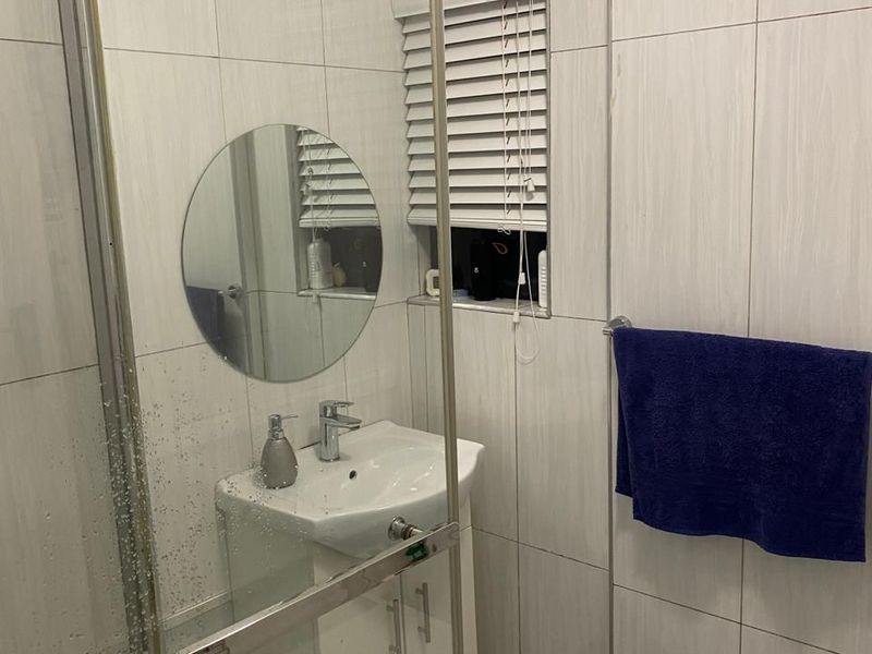 A compact bathroom featuring floor-to-ceiling wall tiles, a modern vanity unit with a basin, and a glass-enclosed shower area.