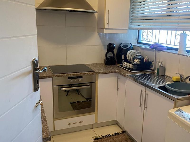 Compact kitchen featuring white cabinetry, stainless steel extractor fan, built-in oven, electric hob, and a stainless steel sink with tiled splashback.