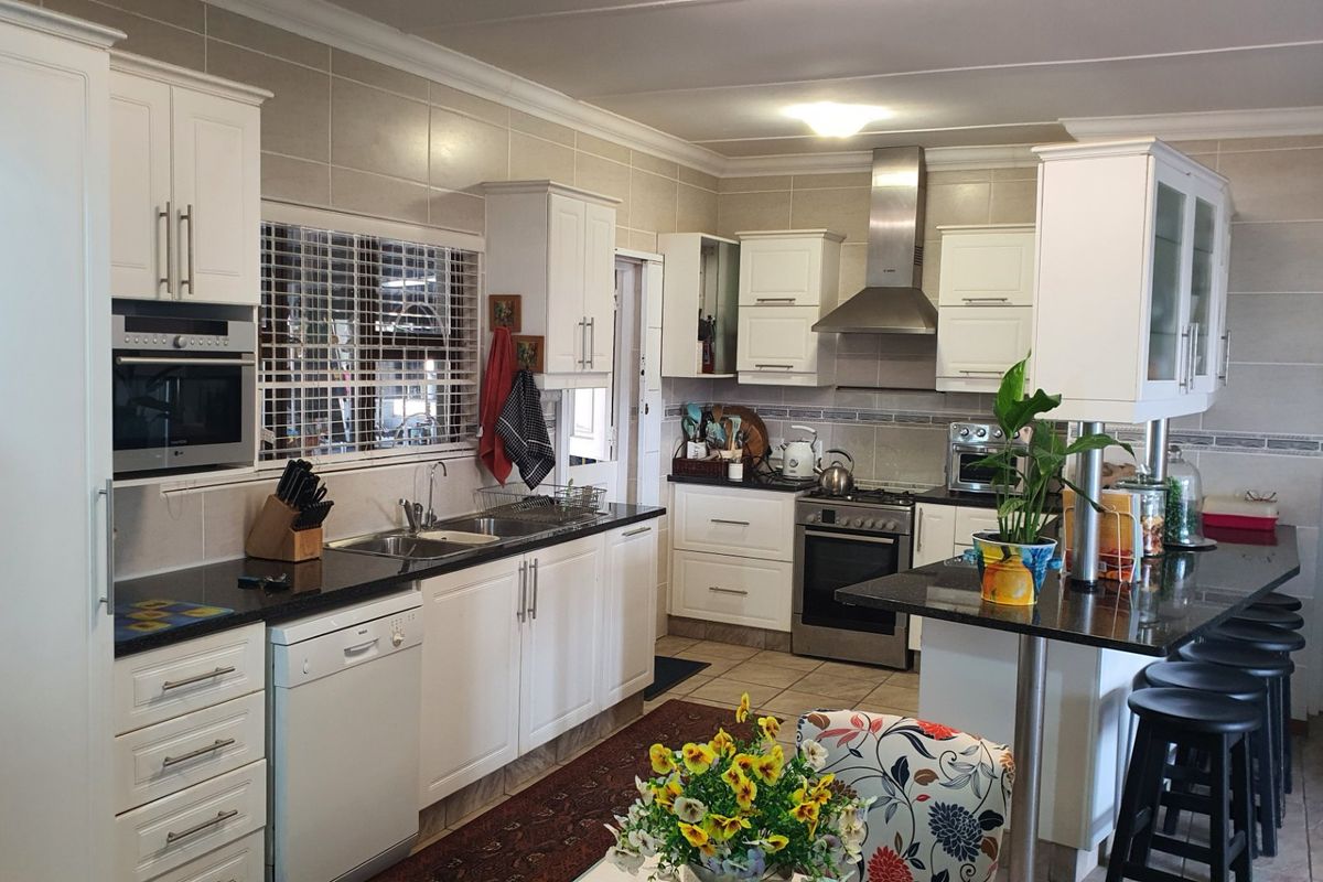 A well-maintained kitchen featuring white cabinetry, granite countertops, stainless steel appliances, a tiled backsplash, and a functional breakfast bar area.