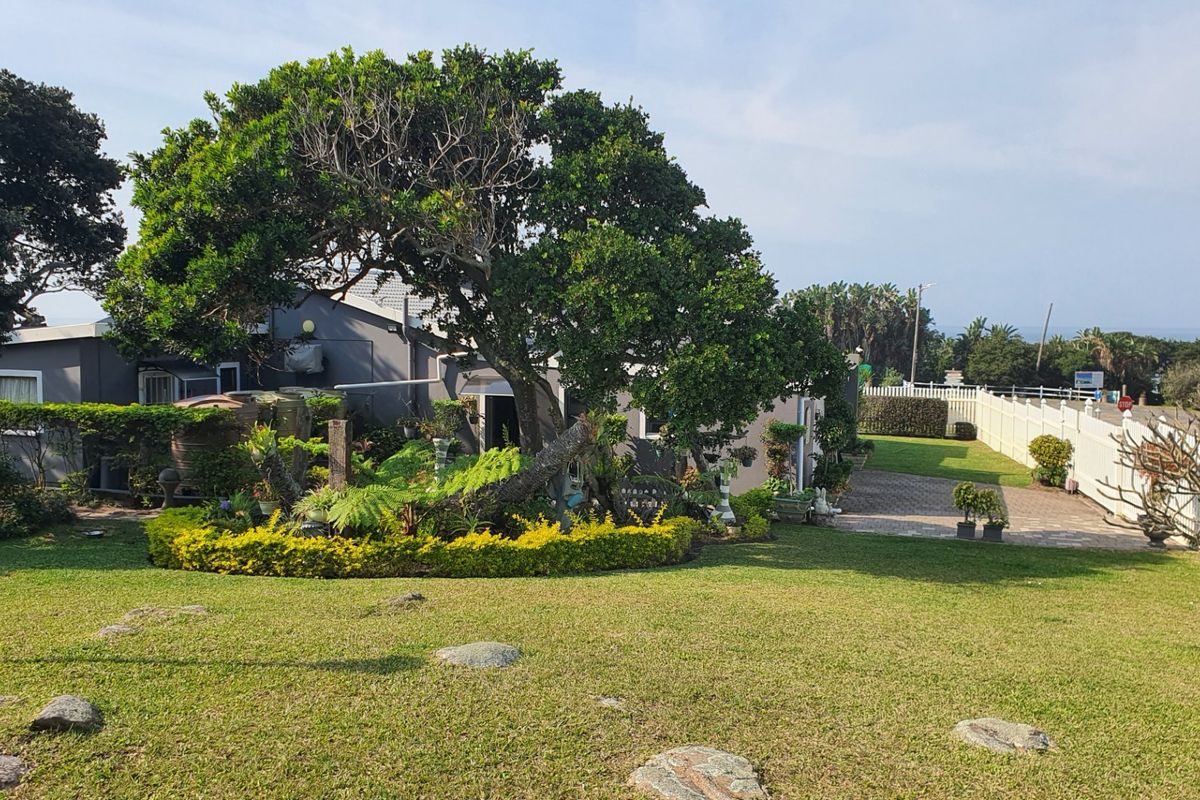 A spacious rear garden featuring a paved driveway, mature trees, landscaped garden beds, and boundary fencing, providing a private outdoor area.
