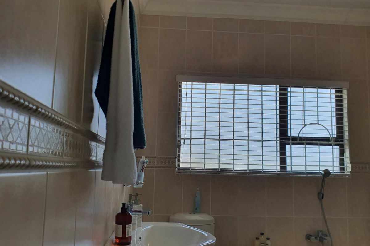 A functional bathroom featuring neutral wall tiling, a pedestal basin, and a window with fitted venetian blinds.