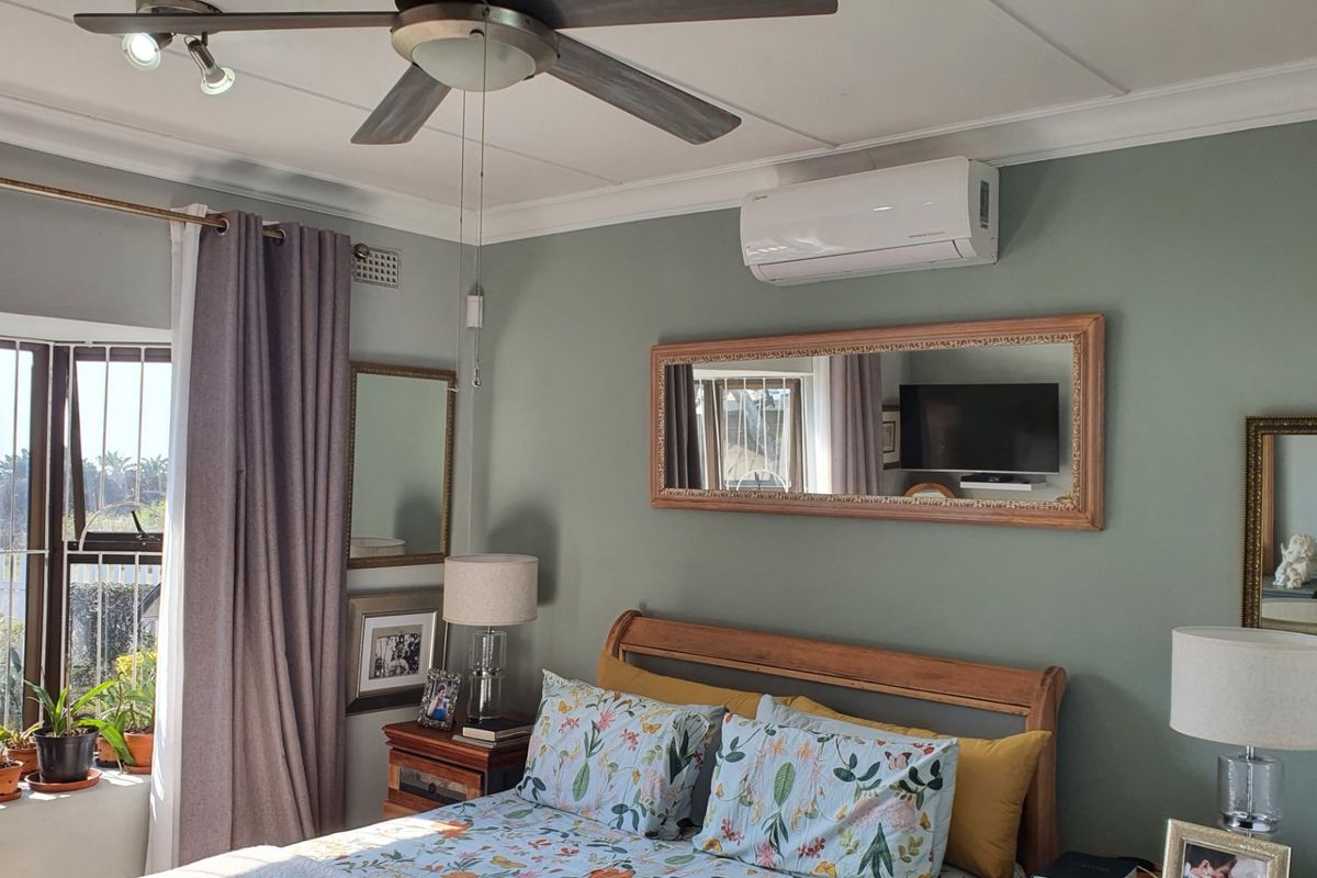 A well-maintained bedroom featuring a ceiling fan, split-system air conditioning, and large windows with security bars, offering a comfortable and functional living space.