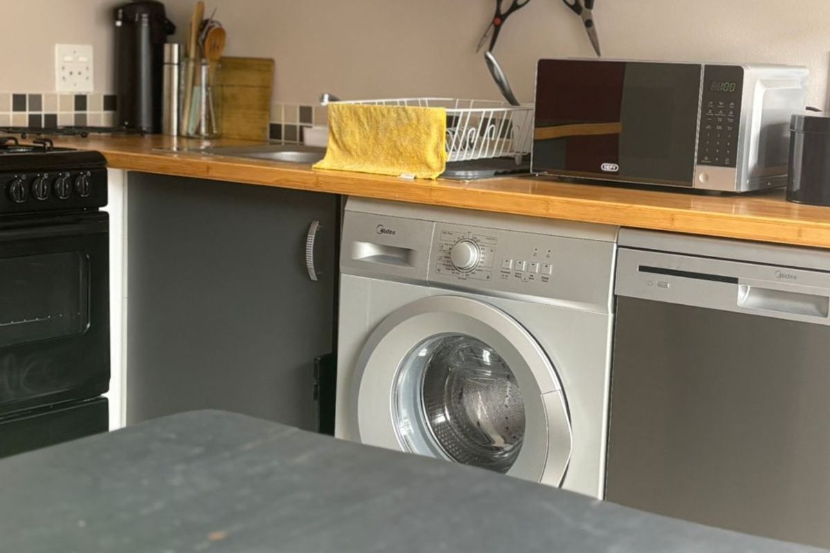A functional kitchen featuring dark cabinetry, wooden countertops, a tiled backsplash, and integrated appliances including a washing machine and dishwasher.