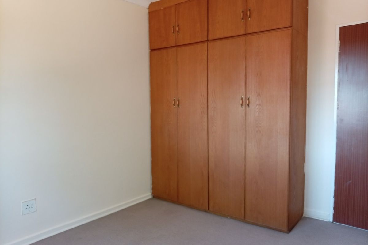 A clean, empty bedroom featuring neutral walls, carpeted flooring, and floor-to-ceiling built-in wooden cupboards for ample storage.