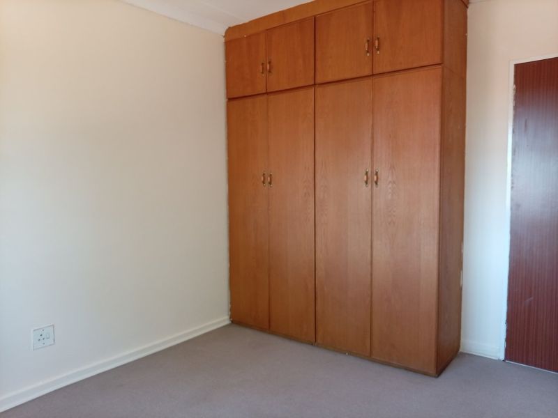 A clean, empty bedroom featuring neutral walls, carpeted flooring, and floor-to-ceiling built-in wooden cupboards for ample storage.