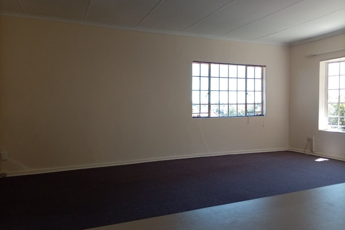 A spacious, empty living area featuring carpeted flooring, grid-pattern windows, and neutral walls, offering a blank canvas for personalization.