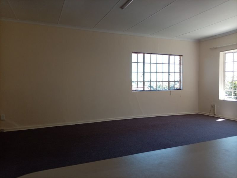 A spacious, empty living area featuring carpeted flooring, grid-pattern windows, and neutral walls, offering a blank canvas for personalization.
