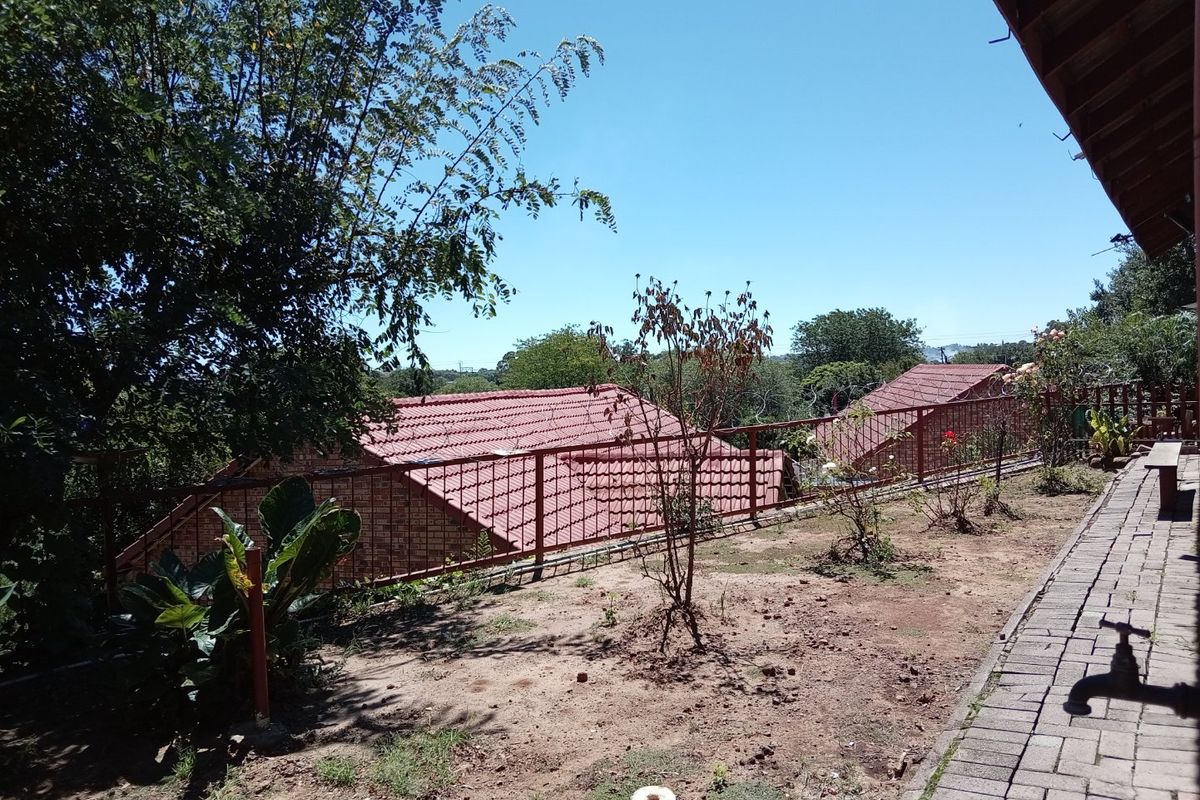 A rear exterior view featuring a paved walkway, metal safety railing, and a view over neighboring tiled roofs.