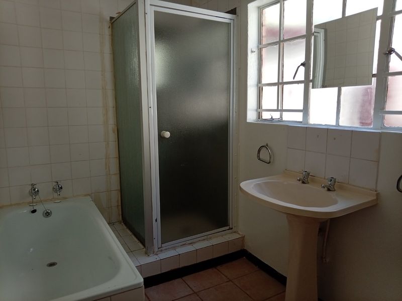A dated bathroom featuring a bathtub, separate shower enclosure, and pedestal basin, requiring cosmetic updates to modernize the space.