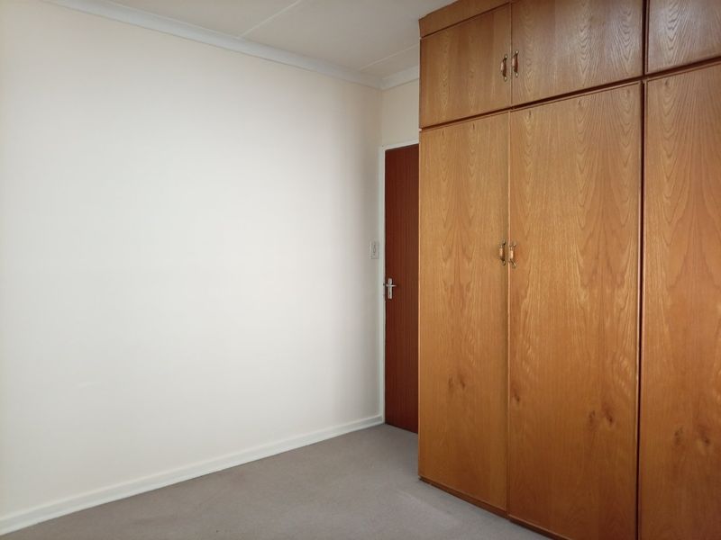 A clean, empty bedroom featuring neutral walls, carpeted flooring, and ample built-in wooden storage cupboards.