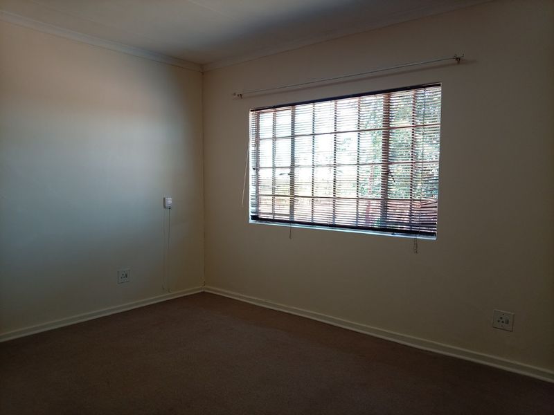 An empty bedroom featuring neutral walls, carpet flooring, and a window fitted with venetian blinds.