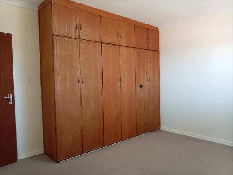 A spacious bedroom featuring extensive built-in wooden cupboards and neutral carpeting, offering a blank canvas for personalization.