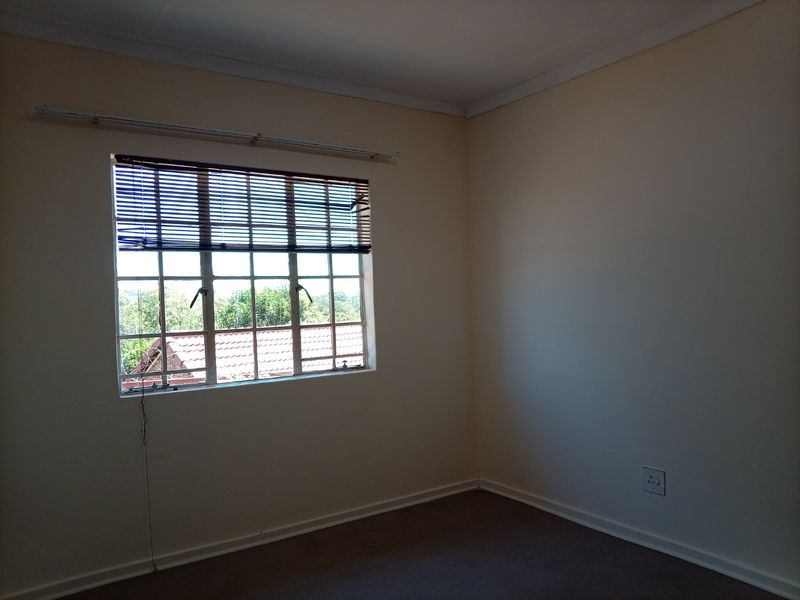 An empty bedroom featuring carpeted flooring, a window with burglar bars and venetian blinds, and neutral wall finishes.