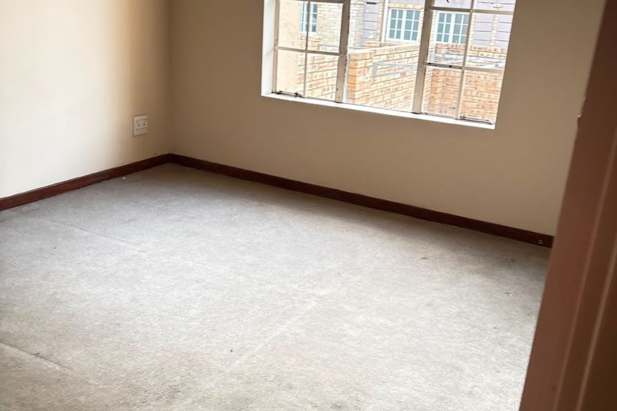 An empty bedroom featuring neutral walls, a grid-pattern window, and carpeted flooring, offering a blank canvas for personalization.