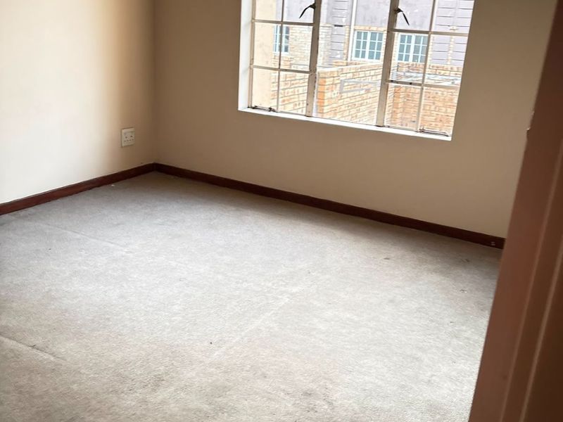 An empty bedroom featuring neutral walls, a grid-pattern window, and carpeted flooring, offering a blank canvas for personalization.