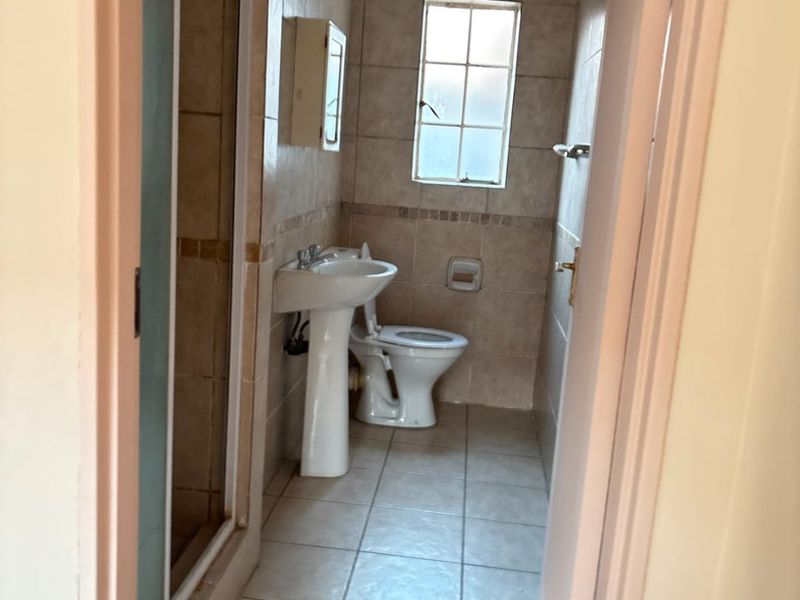 A compact bathroom featuring a pedestal basin, toilet, and shower enclosure with neutral wall and floor tiling.