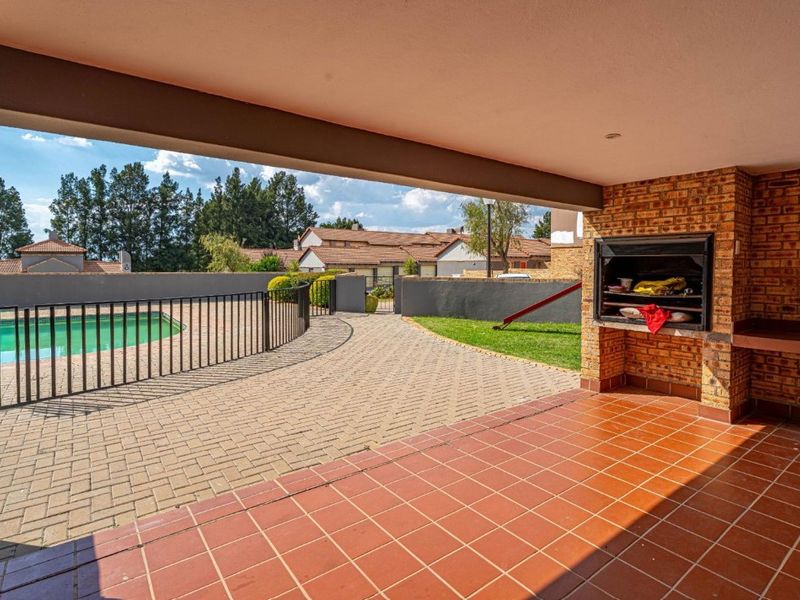 Covered patio area featuring a built-in braai, tiled flooring, and direct access to the paved pool area and garden.