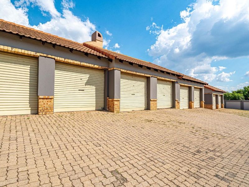 A row of multiple garage units featuring roll-up doors, brick pillars, and a paved driveway in a well-maintained complex setting.
