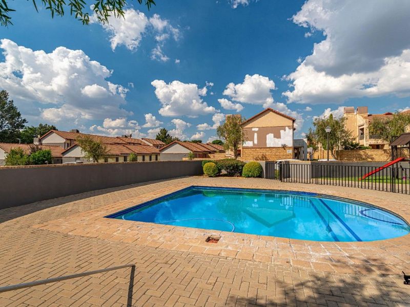Communal swimming pool area featuring a paved deck, perimeter wall, and metal fencing within a residential apartment complex.