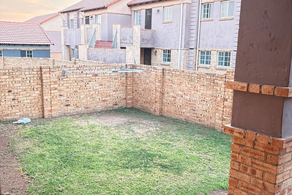 A private rear garden featuring a small lawn, brick boundary walls, and a covered tiled patio area.