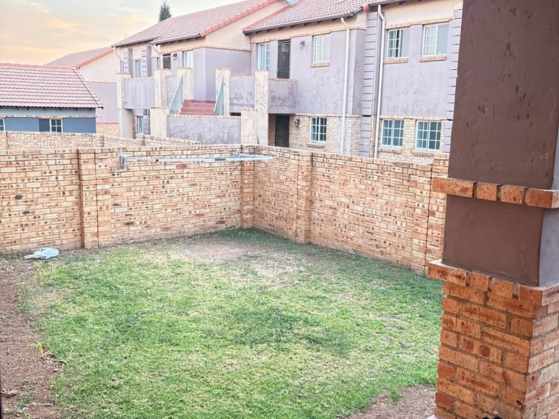 A private rear garden featuring a small lawn, brick boundary walls, and a covered tiled patio area.