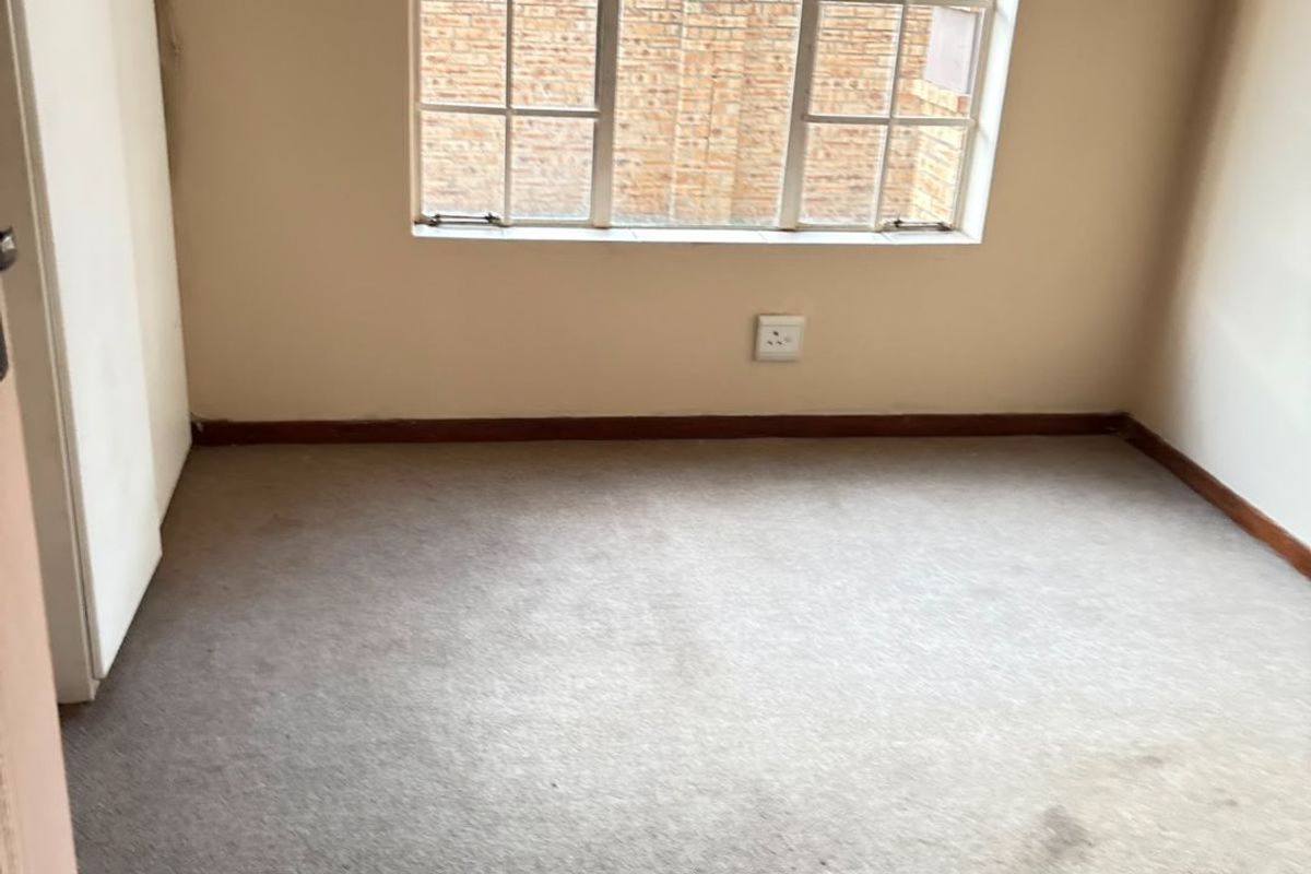 An empty bedroom featuring carpeted flooring, a built-in cupboard, and a window with security bars, offering a blank canvas for potential updates.