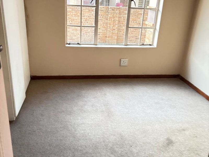 An empty bedroom featuring carpeted flooring, a built-in cupboard, and a window with security bars, offering a blank canvas for potential updates.