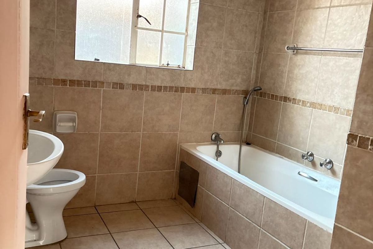 A dated bathroom featuring full-height wall tiling, a standard bathtub with shower mixer, and a toilet. Requires minor repairs to the bathtub apron.