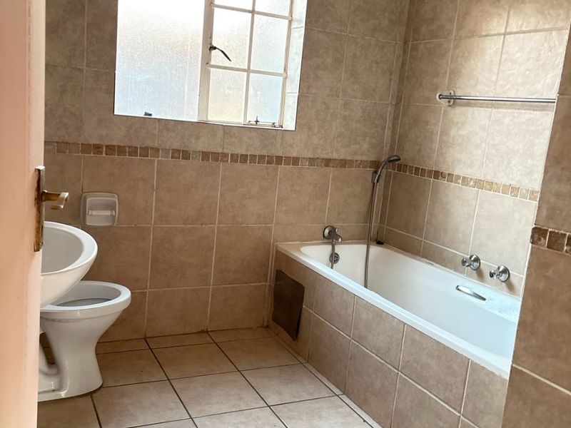 A dated bathroom featuring full-height wall tiling, a standard bathtub with shower mixer, and a toilet. Requires minor repairs to the bathtub apron.