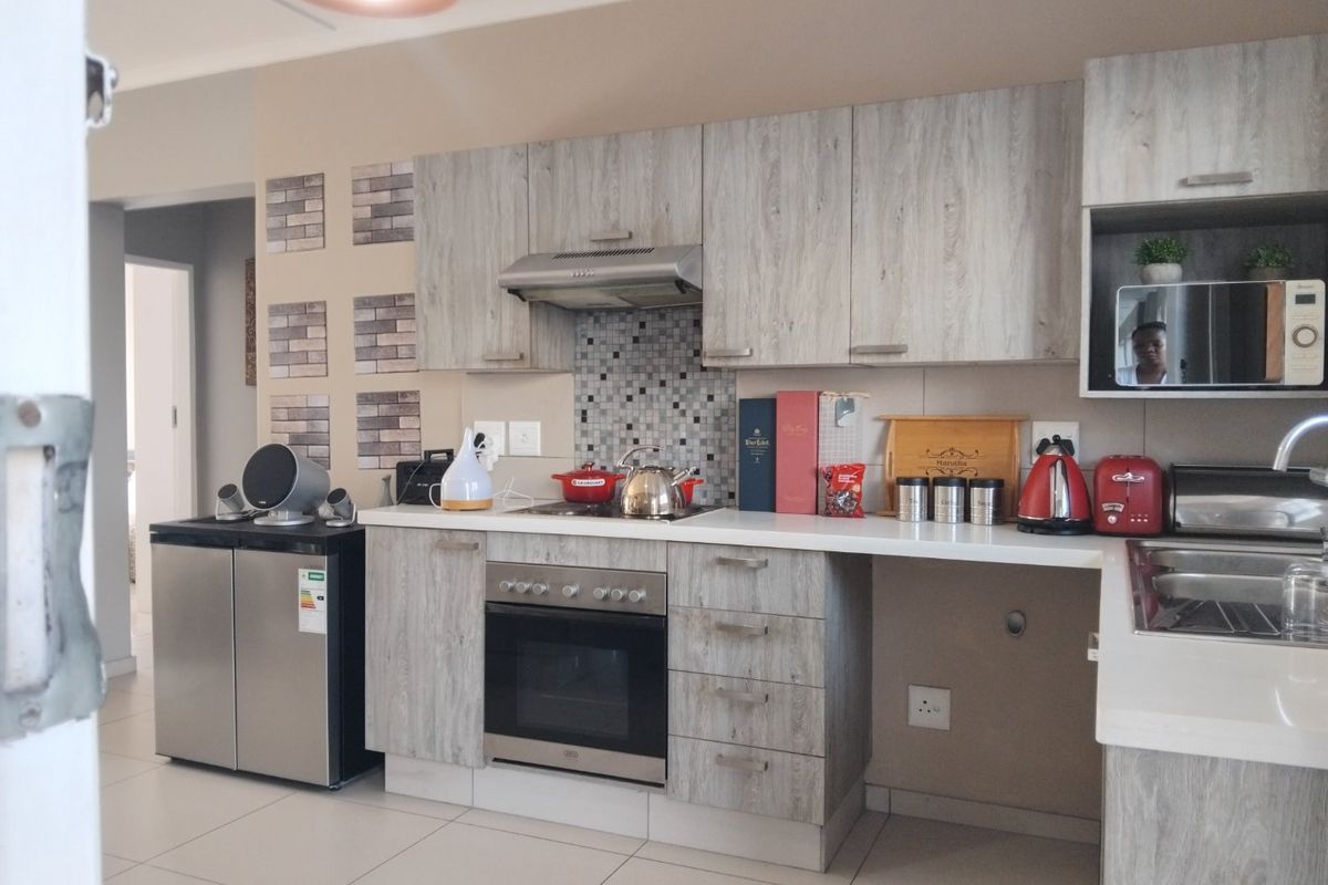 A functional kitchen featuring light wood-grain cabinetry, mosaic tile backsplash, stainless steel oven, and extractor fan with ample counter space.