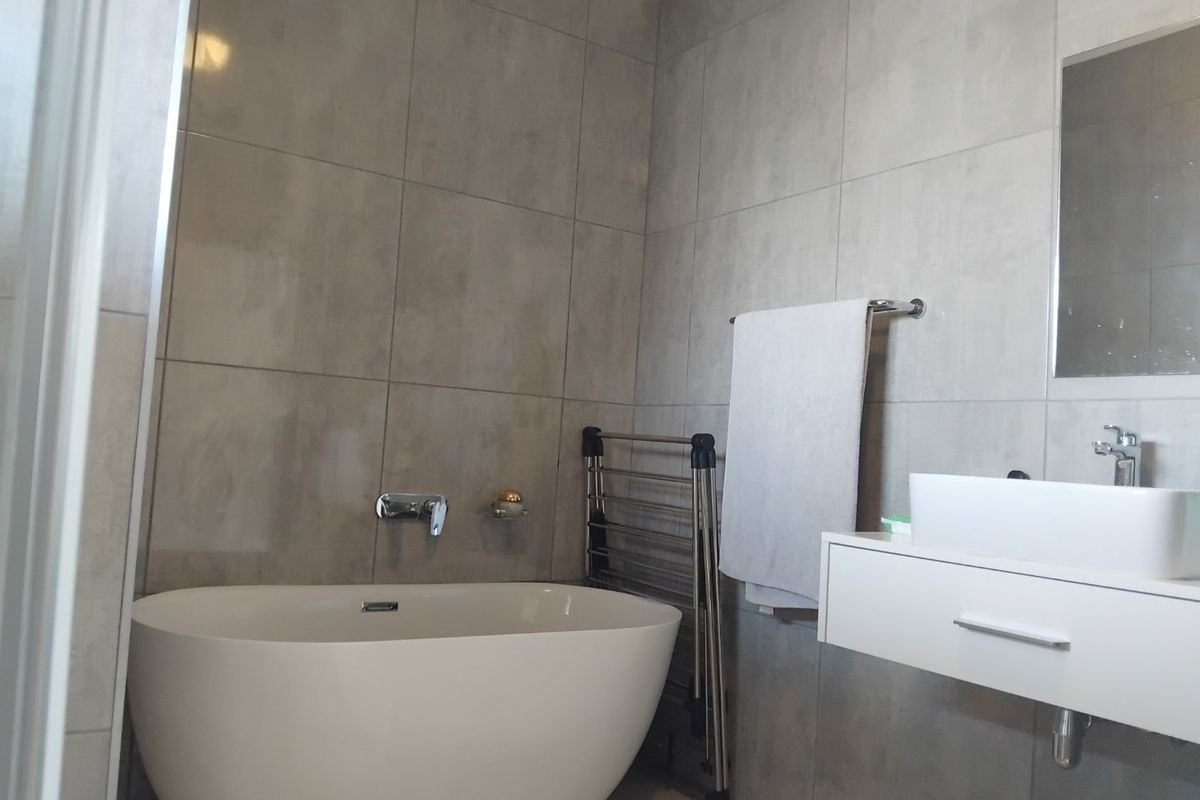 Modern bathroom featuring a sleek freestanding bathtub, wall-mounted basin with chrome fixtures, and contemporary grey wall tiling.