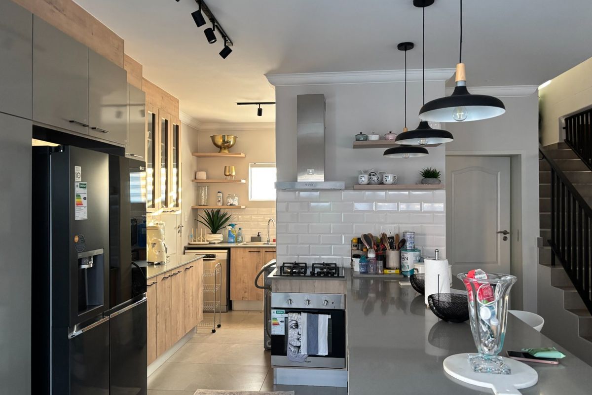 Modern kitchen featuring light wood cabinetry, stone countertops, subway tile backsplash, integrated gas hob, and stylish pendant lighting in an open-plan layout.