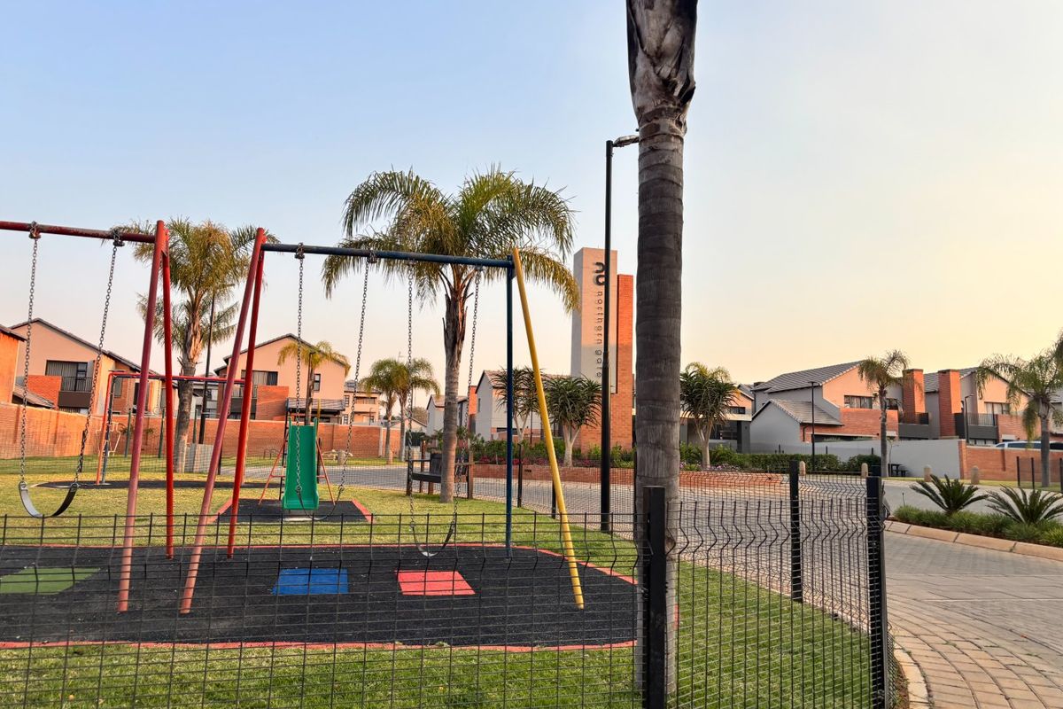 A well-maintained communal outdoor area featuring a playground with swings, landscaped garden spaces, and paved walkways within a residential apartment complex.
