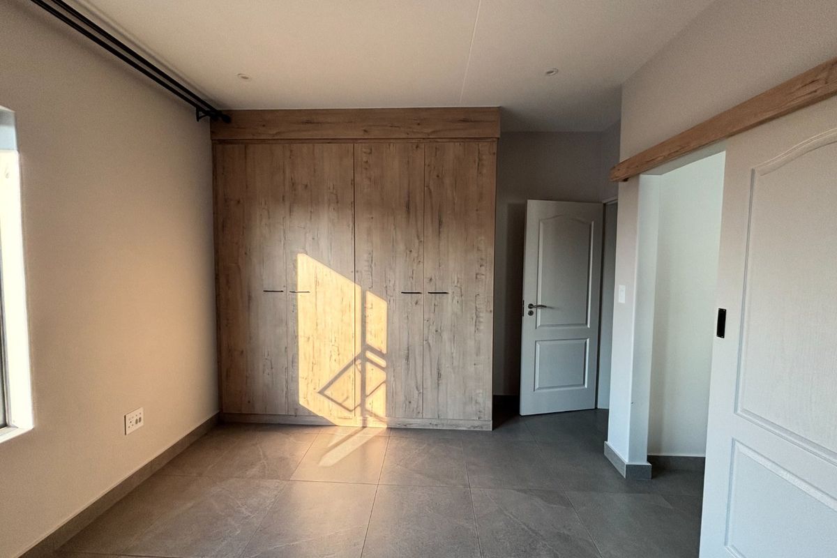 A bright, modern bedroom featuring neutral tiled flooring, built-in wooden cupboards, and clean finishes, offering a versatile space ready for personalization.